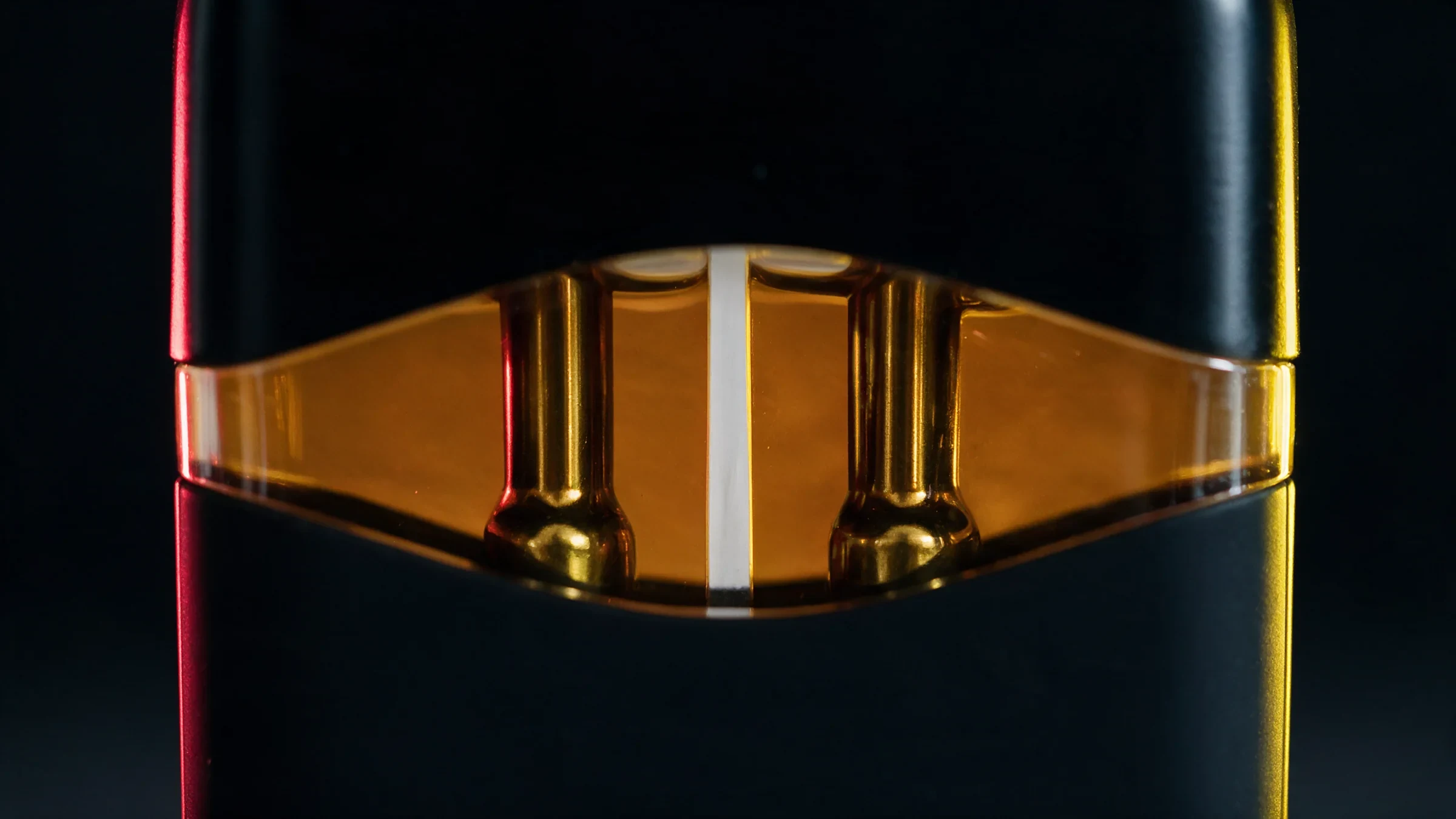 Plano de pormenor da janela âmbar do Penjamin Duo: duas câmaras de óleo com um pino dourado em cada, separadas por uma linha branca fina, com luz vermelha da esquerda e luz amarela da direita